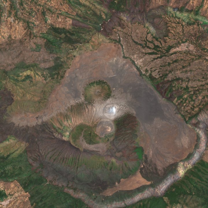 Mount Bromo caldera in true colour: grey sand sea surrounded by green slopes.